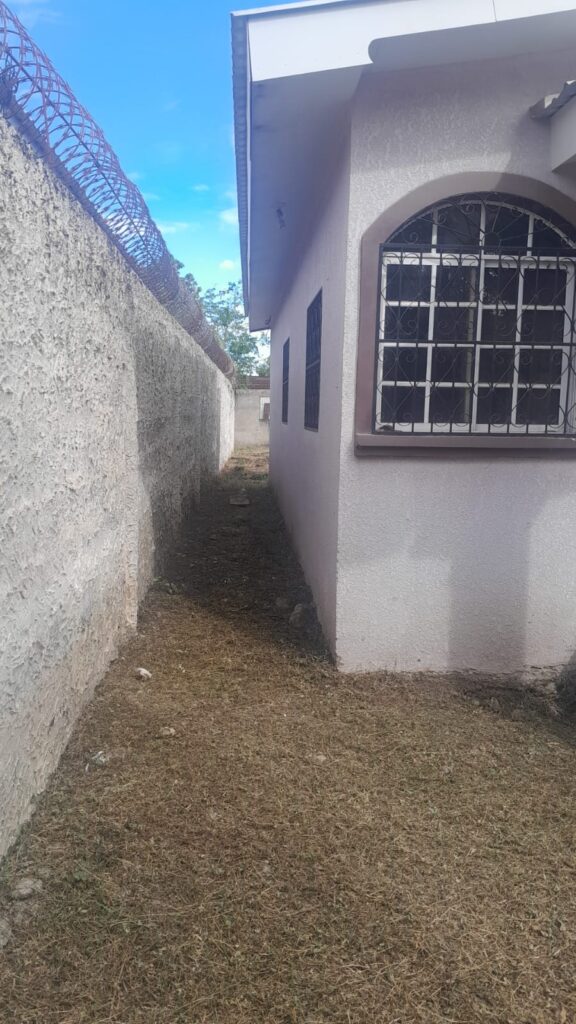 Pasillo lateral de vivienda en venta en Olanchito, con pared perimetral alta y protección de seguridad.