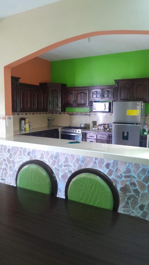 Cocina equipada con barra desayunadora, gabinetes de madera y refrigeradora en espacio iluminado