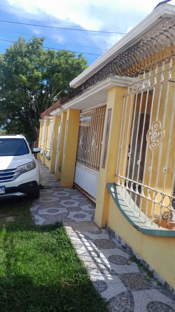 Fachada de casa en venta con portón de seguridad, espacio para vehículo y entrada peatonal con cerámica decorativa.