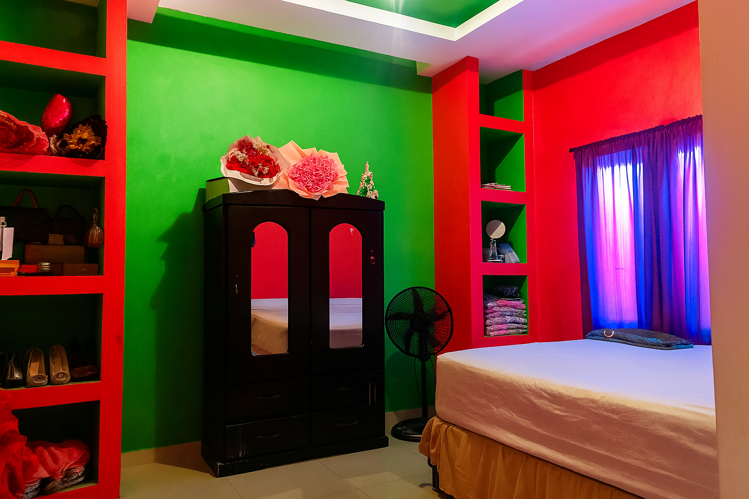 Amplia habitación con paredes color verde y rojo, ropero de madera, cama matrimonial y detalles decorativos.