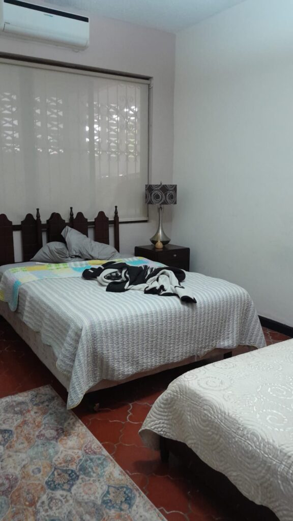Habitación secundaria con dos camas, aire acondicionado y persianas, ideal para visitas o familia.