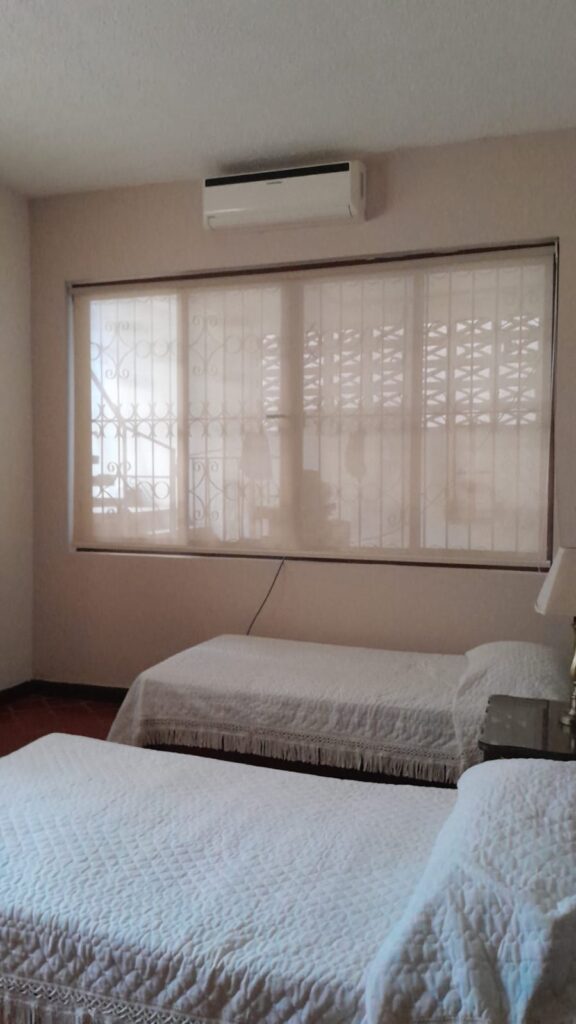 Habitación secundaria con dos camas, aire acondicionado y persianas, ideal para visitas o familia.