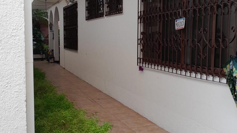 Imagen del acceso y corredor lateral de una casa en venta en Olanchito, ubicada detrás de un local comercial, con verjas de seguridad y diseño colonial.